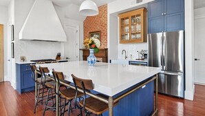 A modern kitchen with a large island, bar stools, a stainless steel refrigerator, and a brick accent wall. - Fab 1838 Garden District 5BR w/Parking & Balcony (New Orleans)