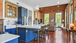 A spacious kitchen with a central island, blue cabinetry, and a brick wall. - Fab 1838 Garden District 5BR w/Parking & Balcony (New Orleans)
