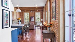 A spacious kitchen with wooden flooring, a dining area with chairs, and a large window providing natural light. - Fab 1838 Garden District 5BR w/Parking & Balcony (New Orleans)