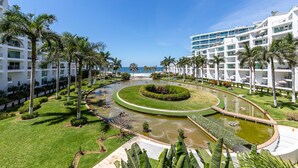 A resort with a central water feature, palm trees, and a view of the ocean.