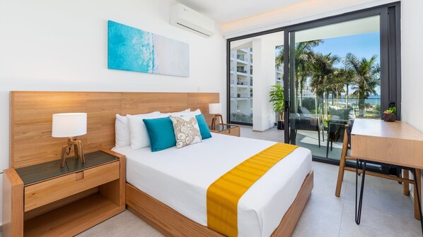 A modern hotel room with a large bed, a desk, and a balcony with a view of palm trees and a building.