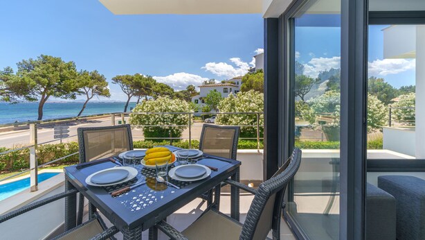 A balcony with a table set for dining, overlooking a pool and a coastal view. - Oratge Beach Views by Interhome (Port Pollença)