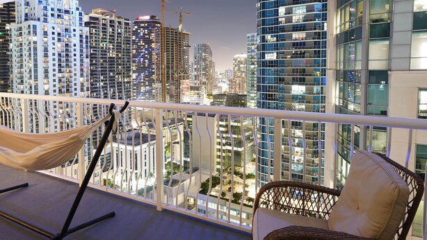 A balcony with a hammock and wicker chair, overlooking a cityscape with high-rise buildings. - 4 bed boho condo with amazing view *Comfortable, stylish and clean* (Miami)