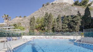 Una piscina amb escales, una palmera i un turó ple d'arbres i un edifici al fons.