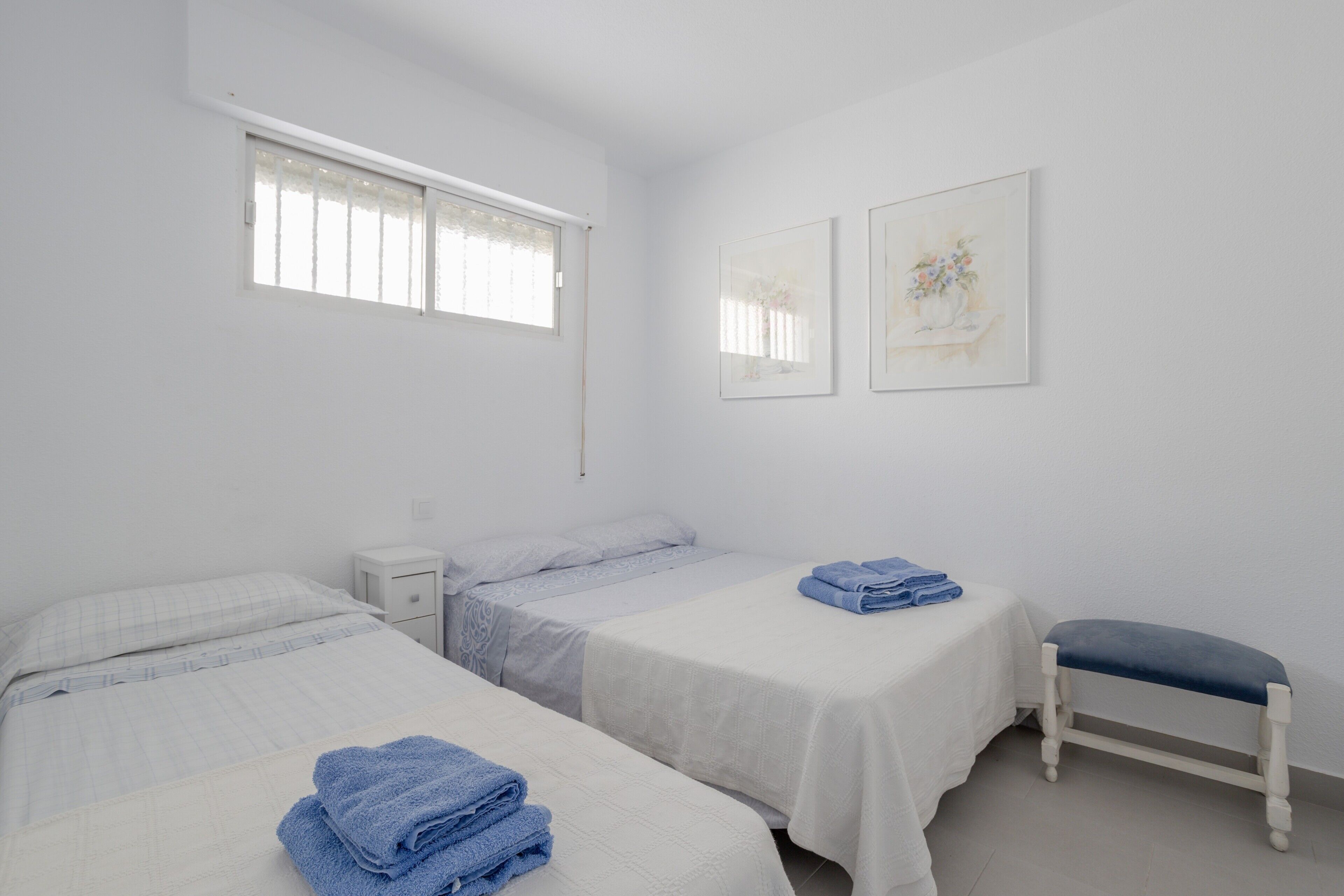 Une chambre d’hôtel propre et minimaliste, avec deux lits, un banc et des œuvres d’art accrochées aux murs.