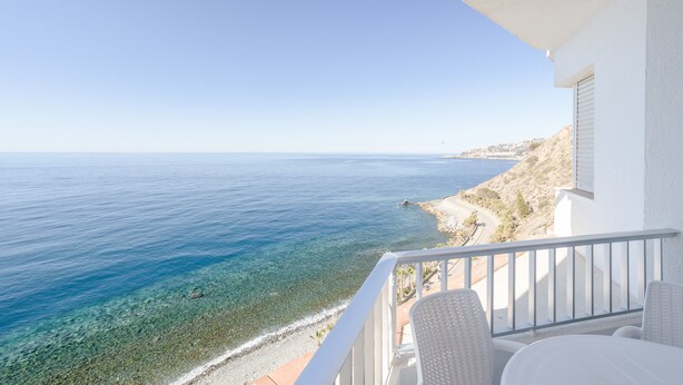 Un balcó amb una vista despejada del mar, un edifici de color blanc i una platja de sorra.