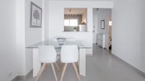 Cuina moderna amb armaris blancs, una finestra i zona de dinar amb taula de vidre i cadires blanques.