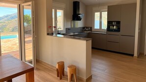 A modern kitchen with a large island, wooden stools, and a view of a pool. - Villa 'Casa Livernana' with Sea View, Wi-Fi and Air Conditioning (Cómpeta)