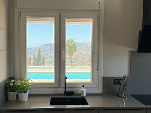 A kitchen with a window overlooking a pool and hills.