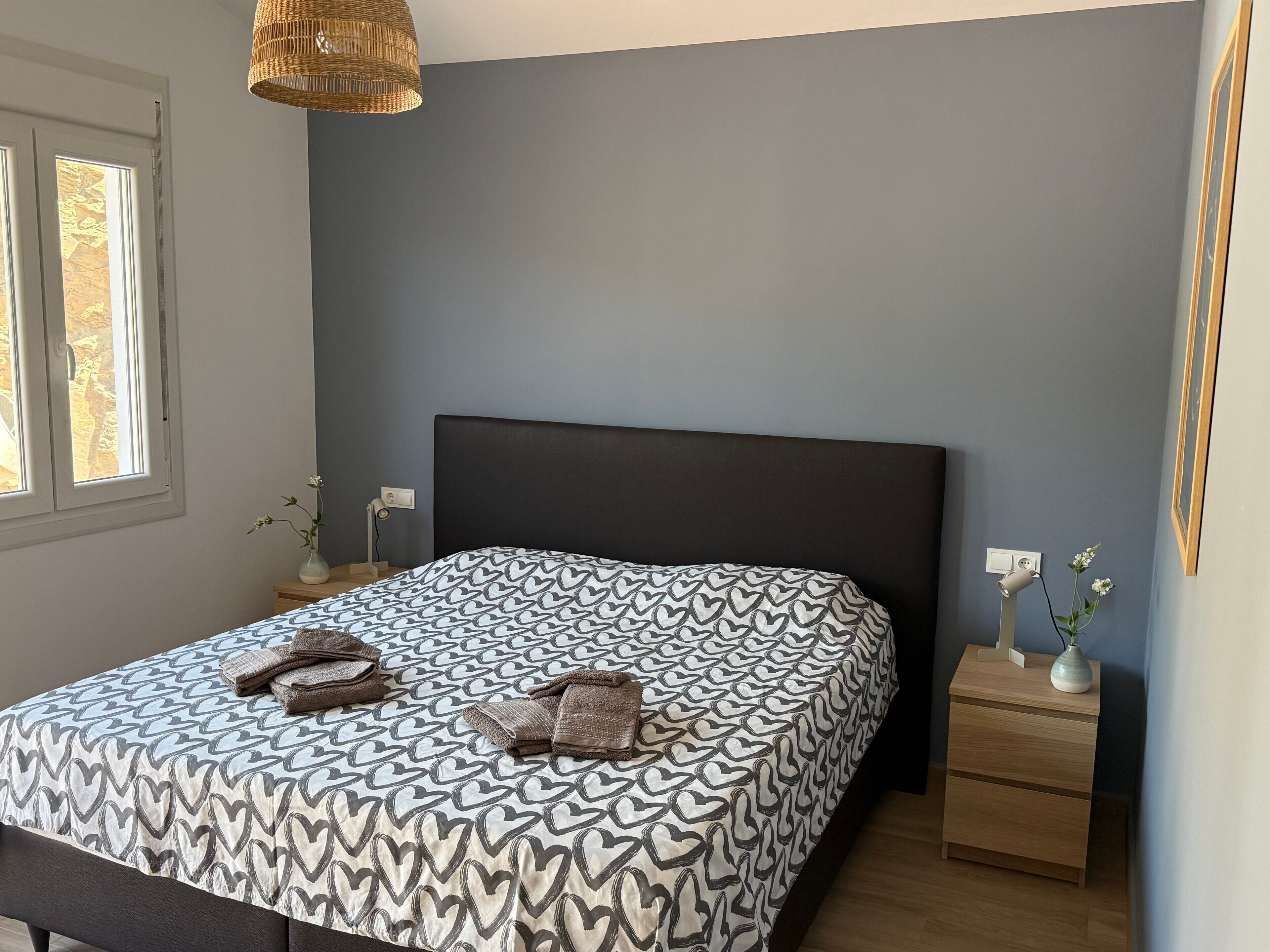 Un dormitorio con cama, mesitas de noche, lámpara y ventana.