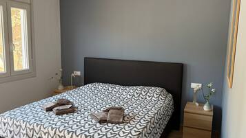 Un dormitorio con cama, mesitas de noche, lámpara y ventana.