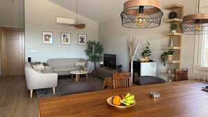 A modern living room with a sofa, coffee table, and dining table. There are pendant lights, a flat-screen TV, and a fireplace. - Villa 'Casa Livernana' with Sea View, Wi-Fi and Air Conditioning (Cómpeta)