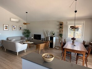 A modern living room with a sofa, TV, dining table, and chairs.