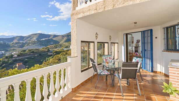 A balcony with a table and chairs, a view of a valley, and a building with a white facade and blue shutters. - "Villa María" with Sea View, Garden, Balcony & Wi-Fi (Almunecar)