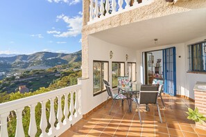 A balcony with a table and chairs, a view of a valley, and a building with a white facade and blue shutters. - "Villa María" with Sea View, Garden, Balcony & Wi-Fi (Almunecar)