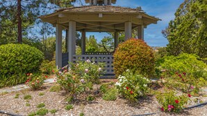 Un gazebo con tetto in tegole, circondato da un giardino con diverse piante fiorite e arbusti.