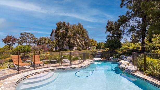 Una piscina con bordo curvo, circondata da un solarium in pietra e lettini prendisole in legno.