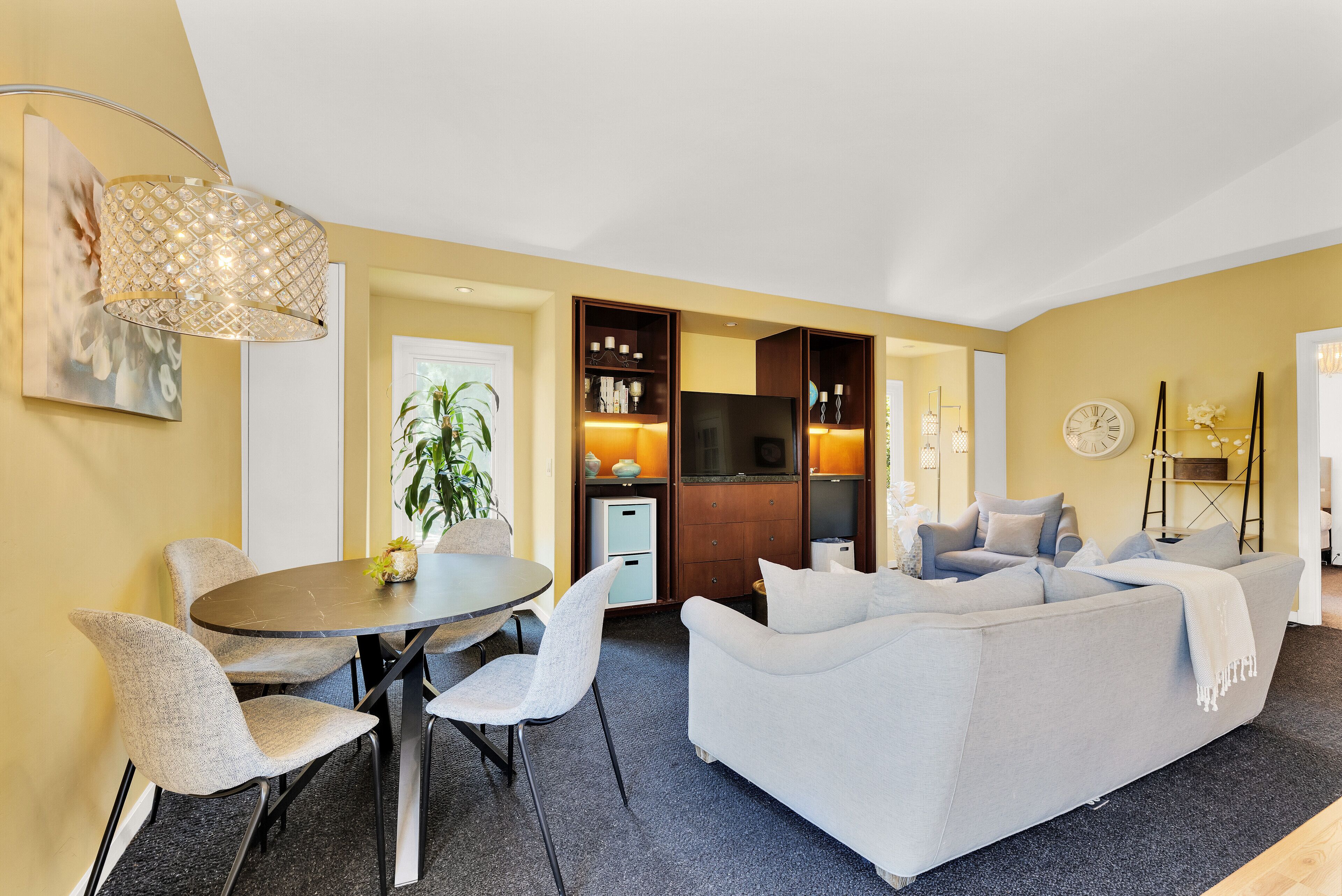 A modern living room with a grey sofa, a round dining table with chairs, a TV, and a decorative lamp.