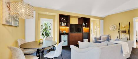 A modern living room with a grey sofa, a round dining table with chairs, a TV, and a decorative lamp.