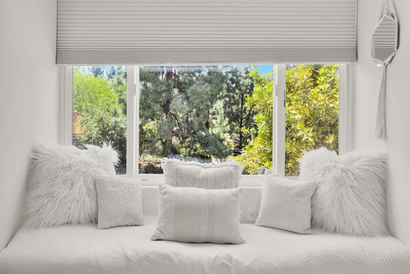 A bedroom with a large window, white bedding, and fluffy pillows.