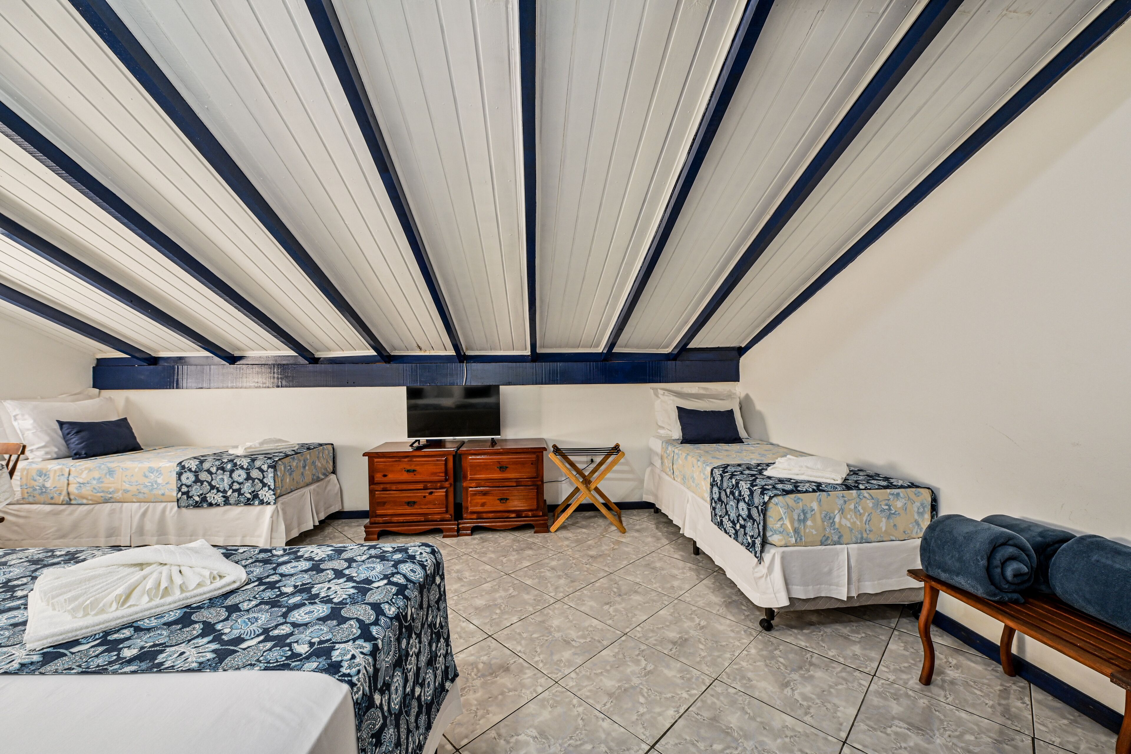Una habitación con dos camas, un aparador de madera, un televisor y un ventilador de techo.