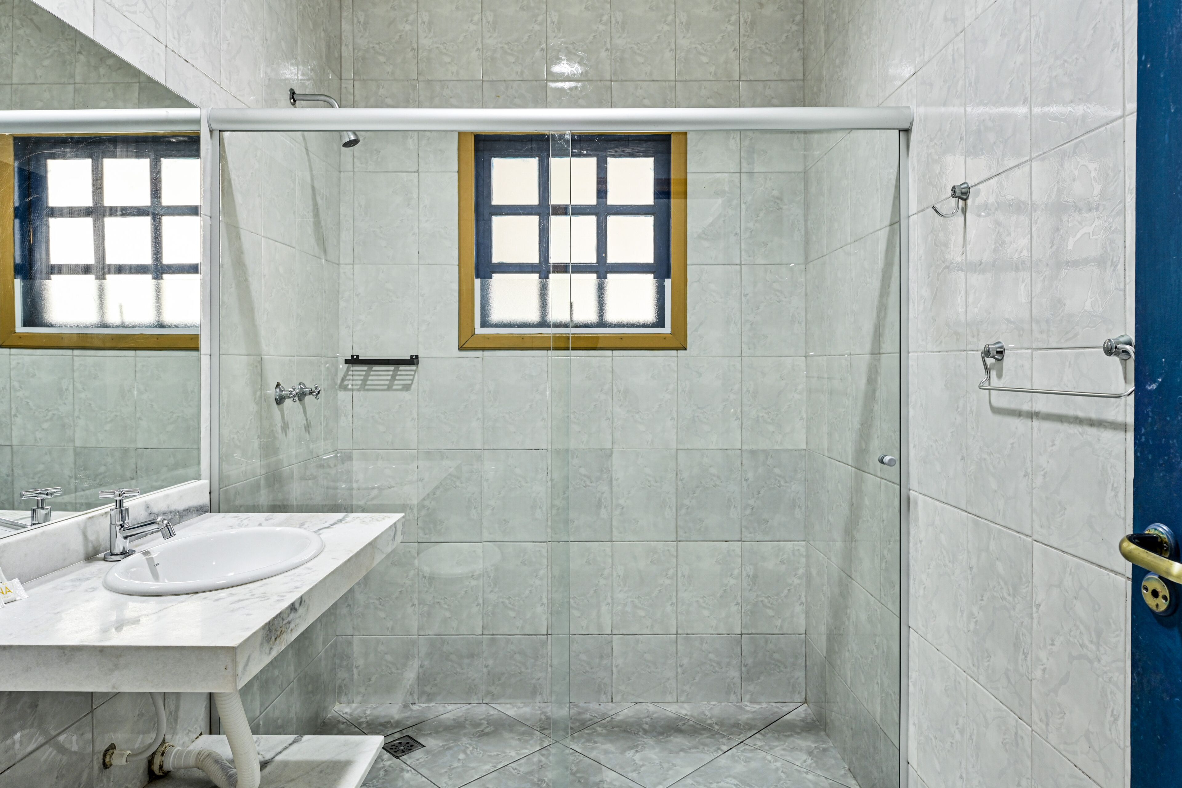 A bathroom with a sink, mirror, shower, and a window.
