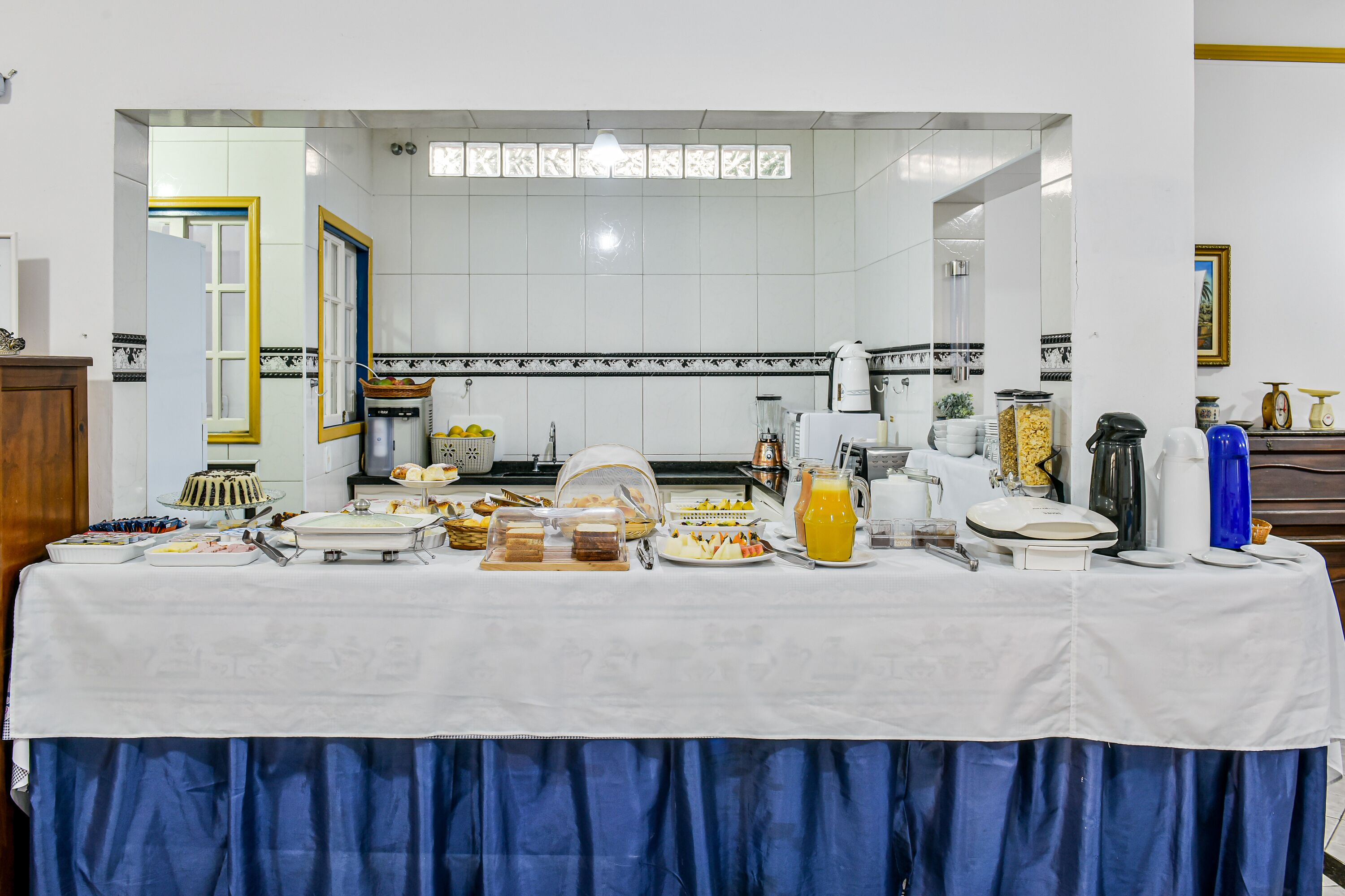 A buffet setup with various food items and beverages, a coffee machine, and a refrigerator in the background.