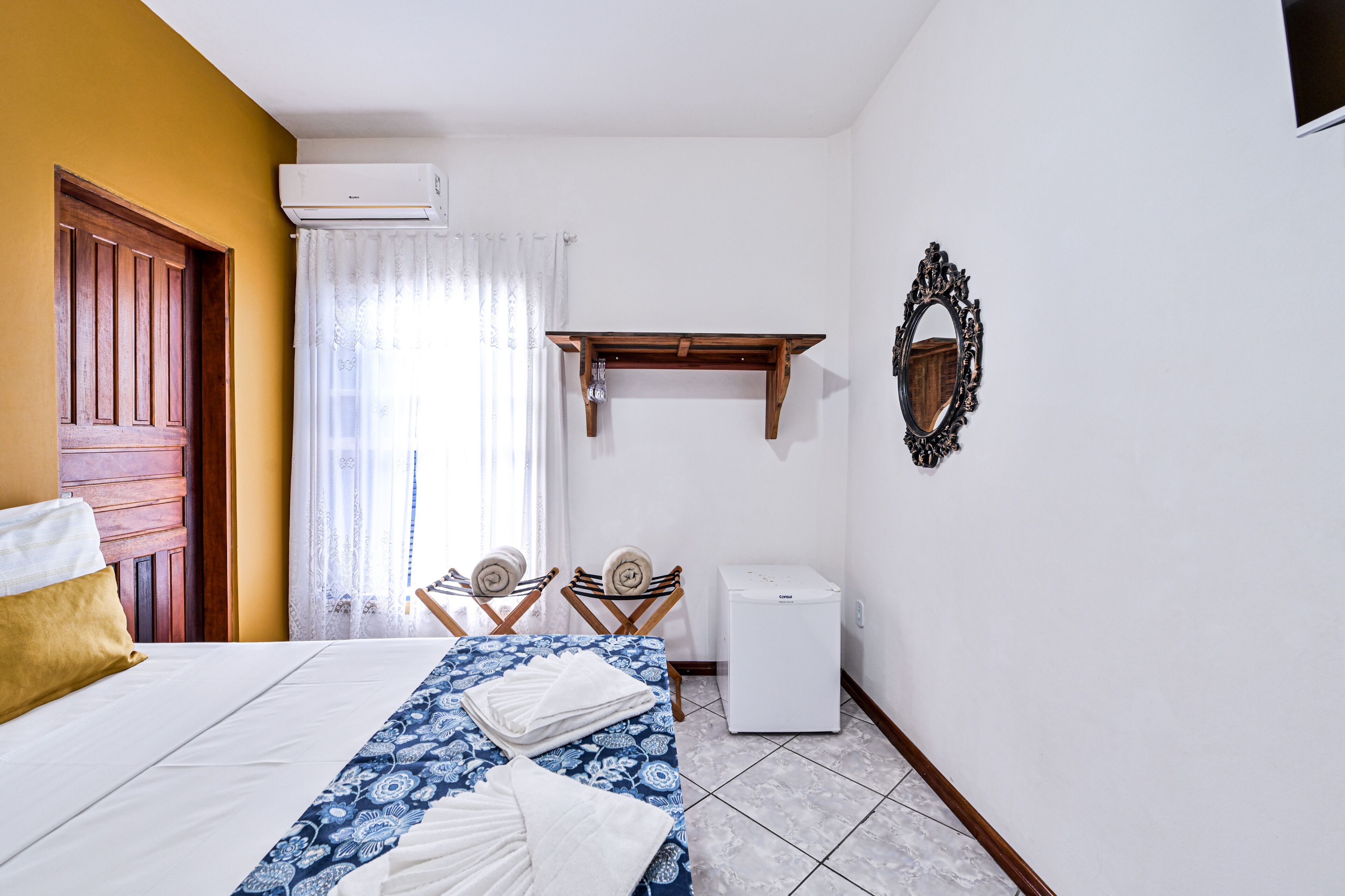 Una habitación de hotel con una cama, una pequeña mesa con sillas, un aire acondicionado blanco y un espejo en la pared.