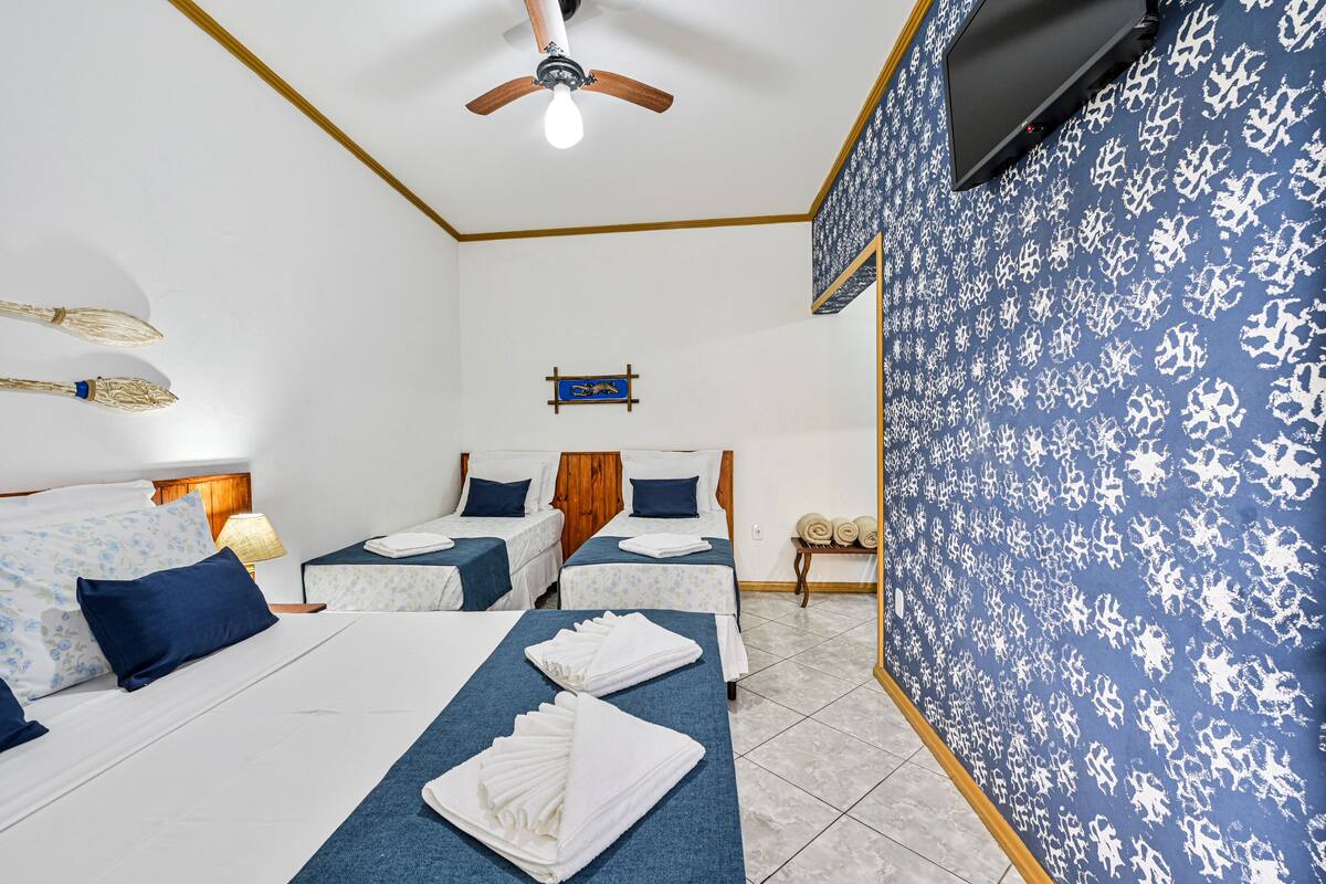 A hotel room with two beds, a ceiling fan, a TV, and a patterned wall.