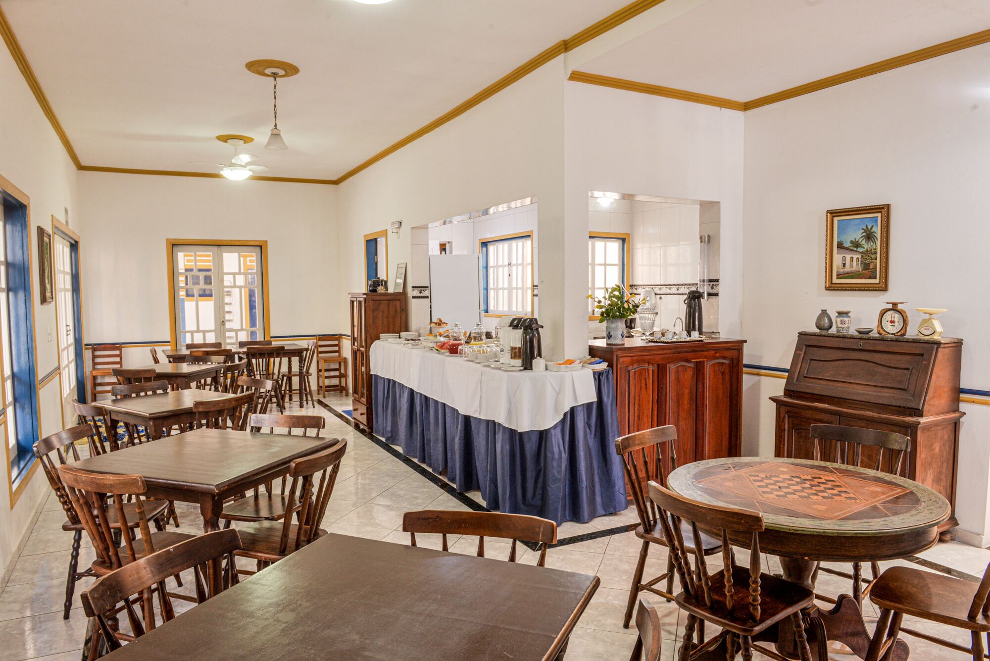 A dining area with wooden tables and chairs, a central buffet table, and a kitchen area with a stove and sink.