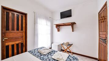 Un dormitorio con una cama, un televisor montado en la pared y un armario de madera.