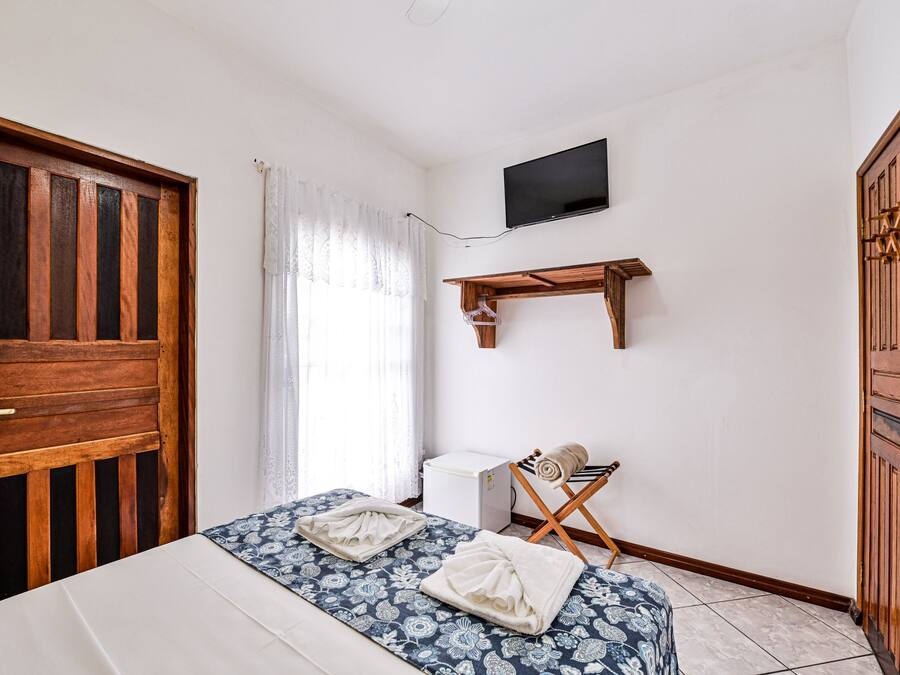 Un dormitorio con una cama, un televisor montado en la pared y un armario de madera.
