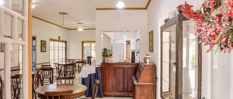A spacious dining area with wooden tables and chairs, a central bar area with a counter, and a large mirror on the right.