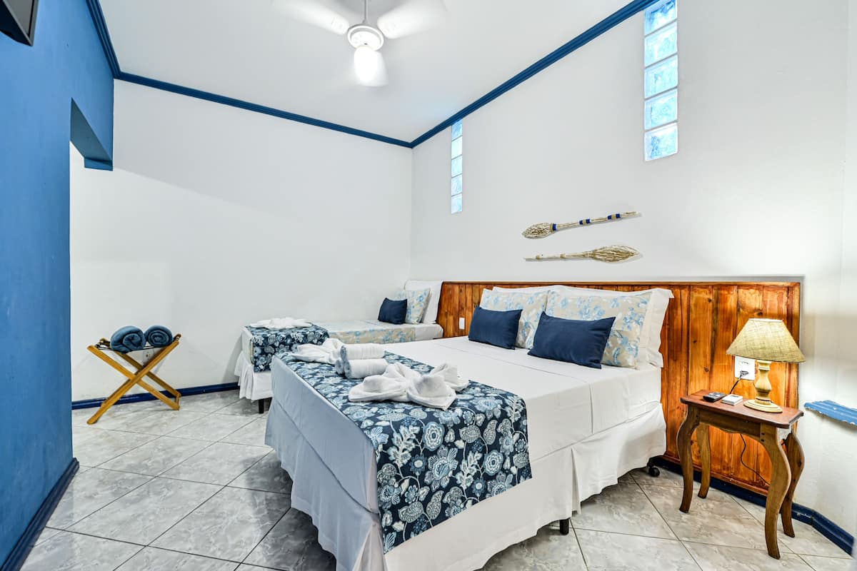 A hotel room with two beds, a wooden headboard, a ceiling fan, a small table with a lamp, and a window with a view.
