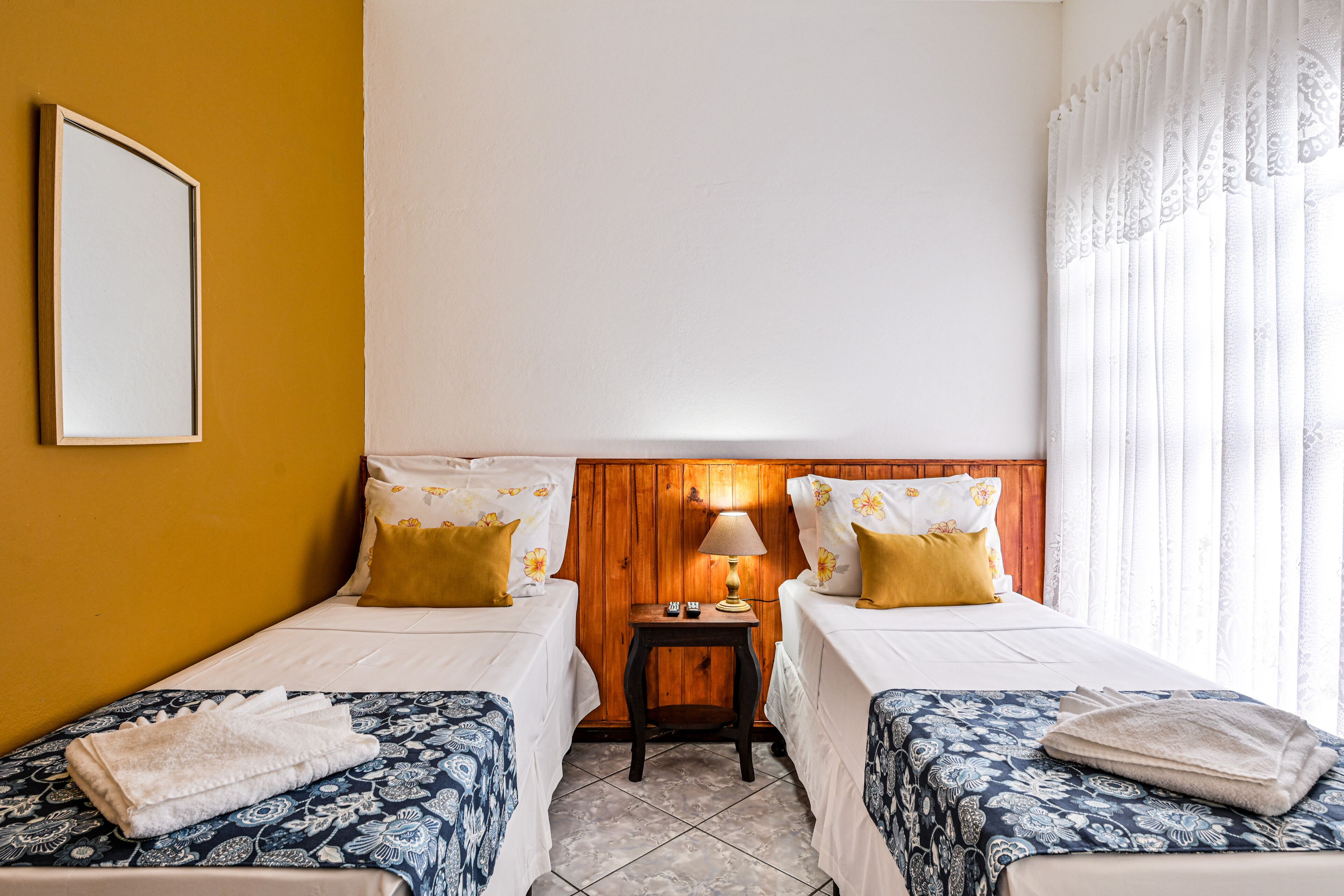 Una habitación de hotel con dos camas, una mesita de noche con lámpara y un espejo en la pared.