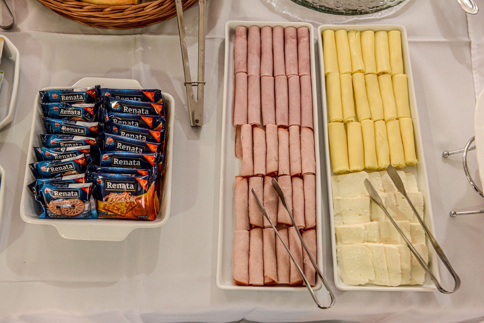 A buffet table with trays of snacks including packaged snacks, sliced meats, and cheese.