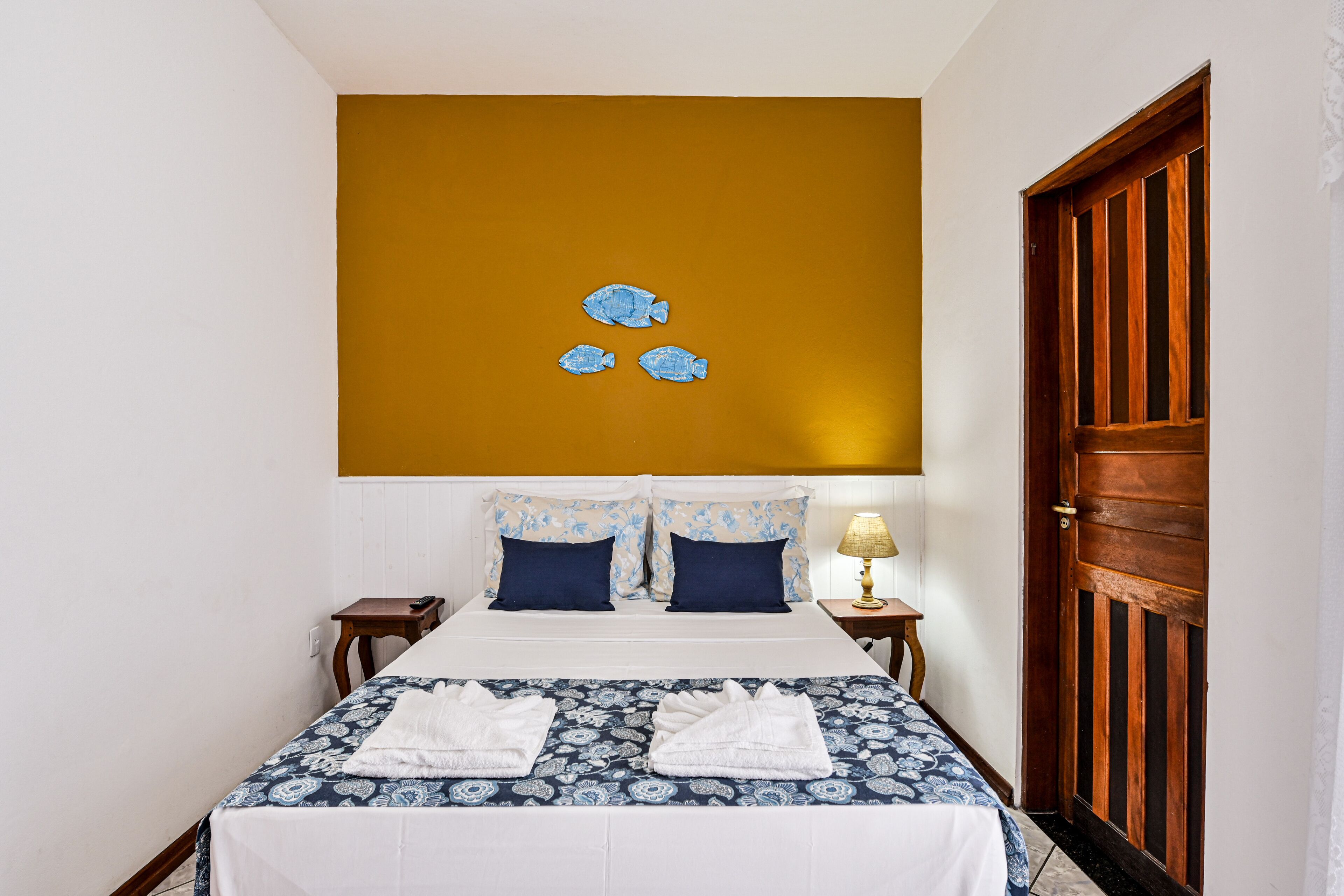 Una habitación de hotel con una cama, dos mesitas de noche, una puerta de madera y una pared con un cuadro de un pez.