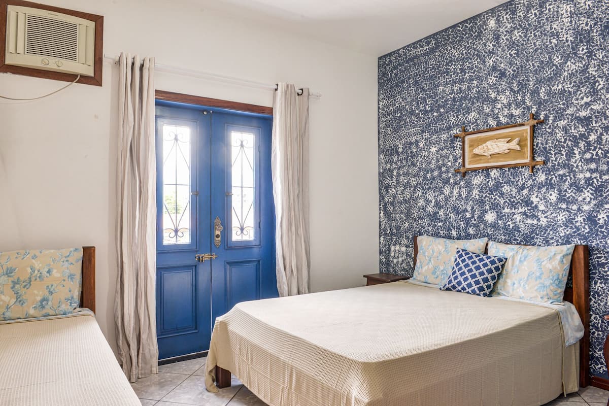 A room with a blue door, a bed with a white bedspread, and a patterned wall.