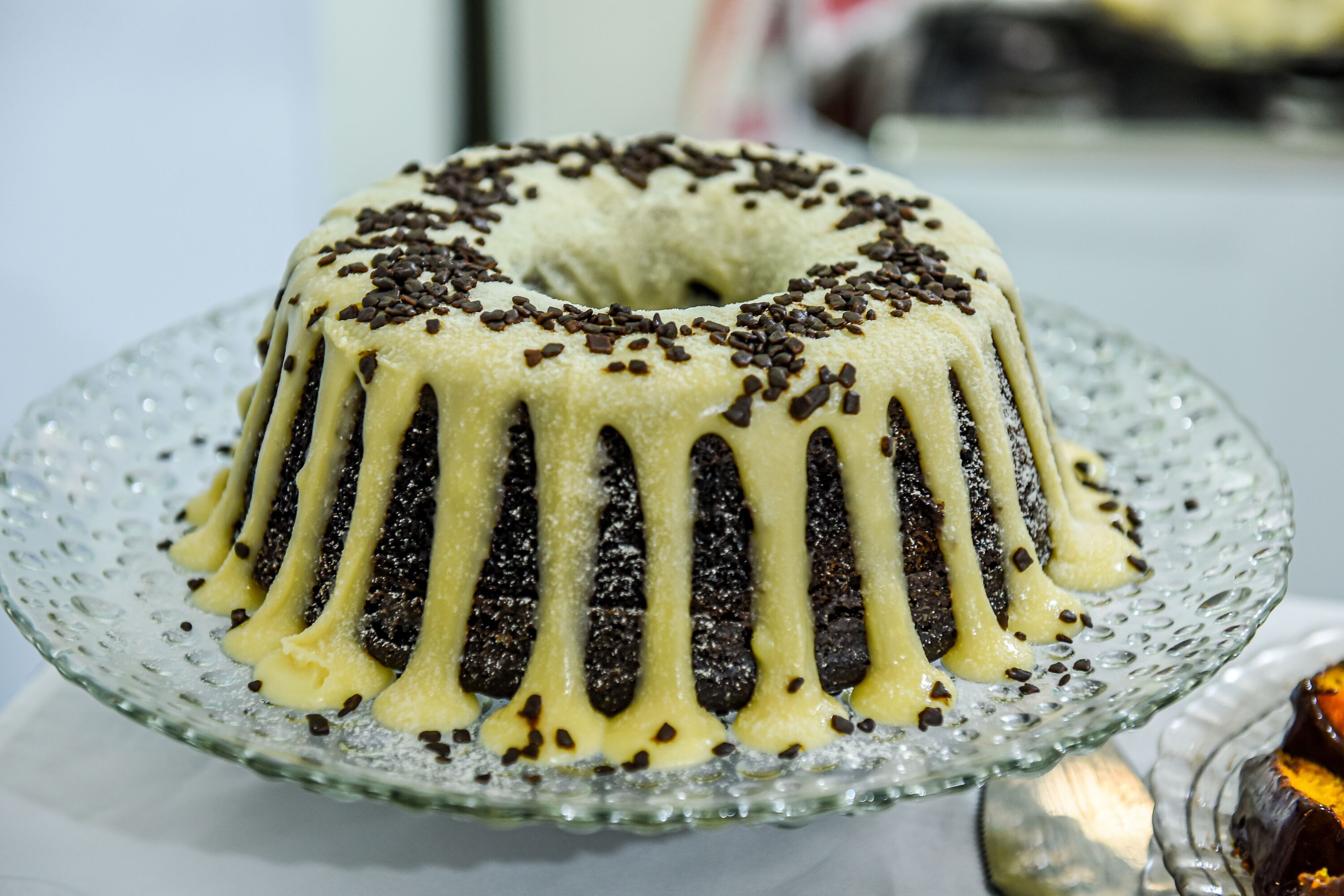 A bundt cake with chocolate drizzle and sprinkles on a glass plate.