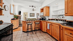 A spacious kitchen with wooden cabinets, a large island with bar stools, a ceiling fan, and a view of the city through a window. - Lakewalk House, near Lake Superior's North Shore and more! (Permit#PL 20140) (Duluth)