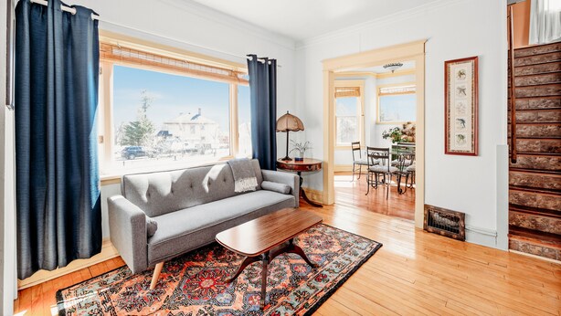 A living room with a sofa, coffee table, and patterned rug. There is a dining area with a table and chairs, and a staircase with a railing. - Lakewalk House, near Lake Superior's North Shore and more! (Permit#PL 20140) (Duluth)