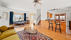 A spacious living room with a sofa, a glass coffee table, and a patterned rug. There is a kitchen area with a bar and stools, and a staircase leading to another level. - Lakewalk House, near Lake Superior's North Shore and more! (Permit#PL 20140) (Duluth)
