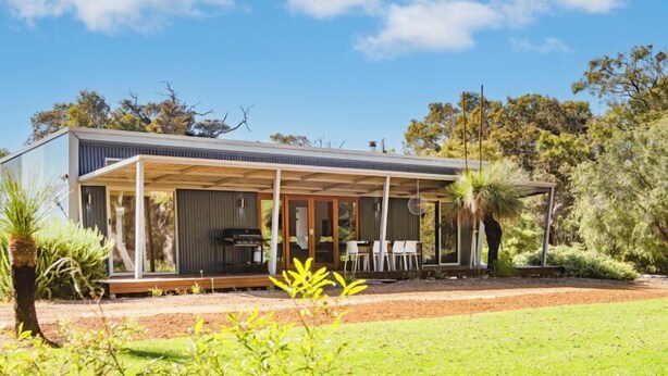 Una casa moderna con un porche cubierto, una zona de barbacoa y un jardín con diversas plantas.