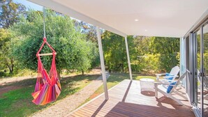 Terraza de madera con sillas colgantes y una mesa, rodeada de vegetación.