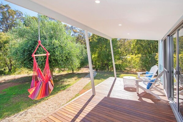 A wooden deck with hanging chairs and a table, surrounded by greenery.