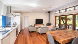 Una cocina moderna con estufa integrada, una zona de comedor con mesa y sillas de madera, y una sala de estar con sofá y televisor.