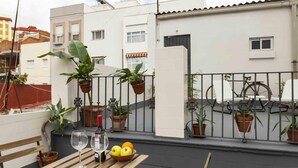 A balcony with a wooden table, two wine glasses, a bowl of fruit, and potted plants. - Apartment 2 rooms-terrace Seville/Triana (Sevilla)