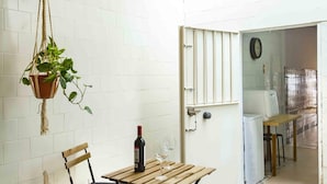 A room with white tiled walls, a hanging plant, a wooden table with a bottle of wine and a glass, and a door leading to another room. - Apartment 2 rooms-terrace Seville/Triana (Sevilla)