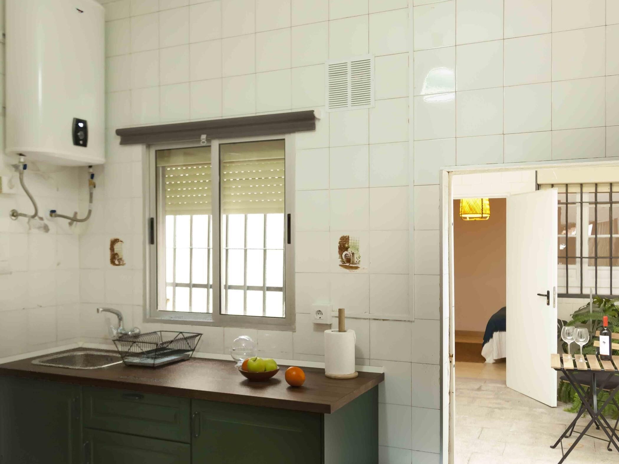 A kitchen with a window, a sink, and a countertop with a bowl of fruit and a roll of paper towels.