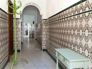 A hallway with patterned tile walls, a green metal stand, and a light-colored table.